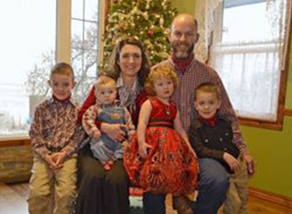 Family of six posing for a Christmas photo indoors near a tree.