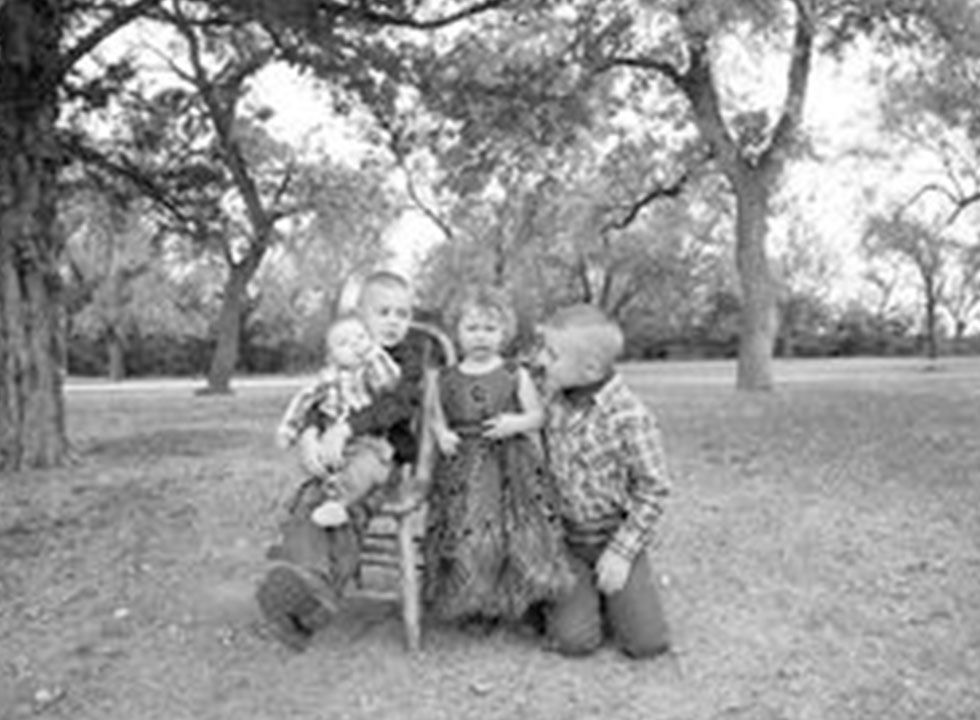 Four young children playing together outdoors under trees.