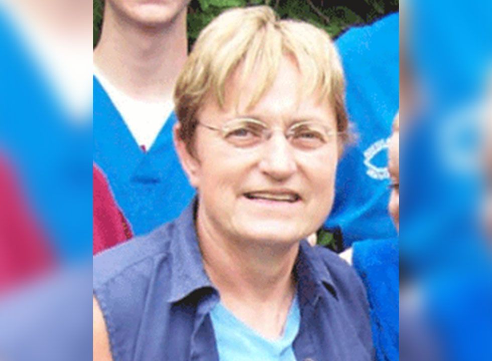 Middle-aged woman with short blond hair wearing glasses and a blue shirt.